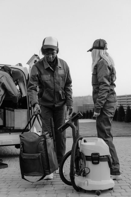 Two professional cleaning technicians from Twickenham Cleaner are preparing equipment outdoors on a paved surface for residential or commercial cleaning tasks. One technician is adjusting a portable v