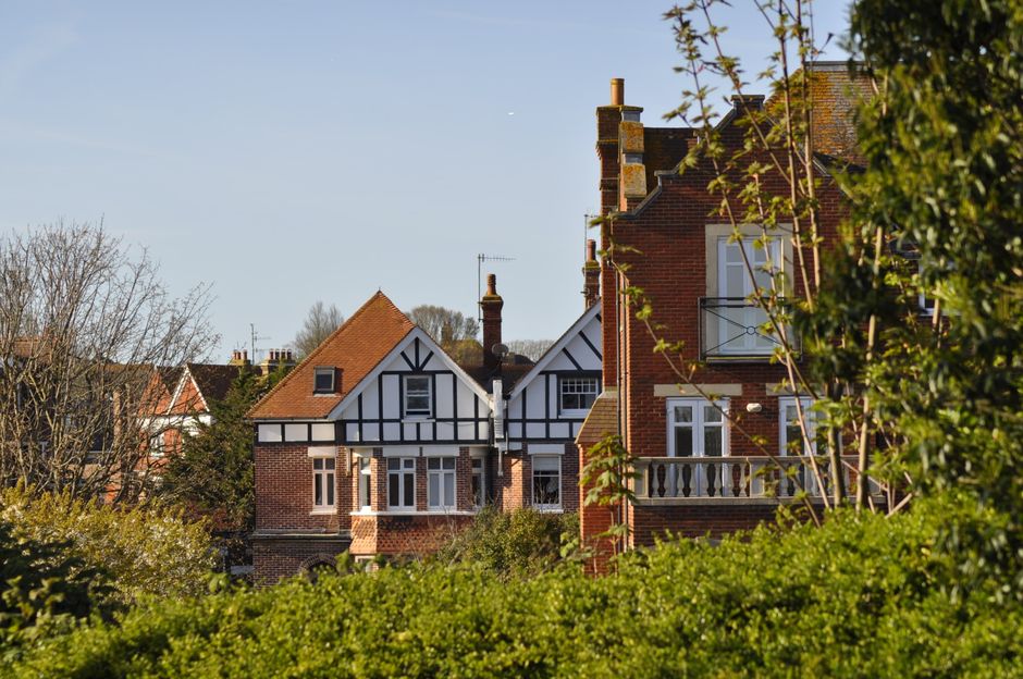 A white Victorian-style building with multiple rectangular sash windows, decorative moldings, and balcony railings, set against a bright blue sky with scattered white clouds and a soaring bird. The bu